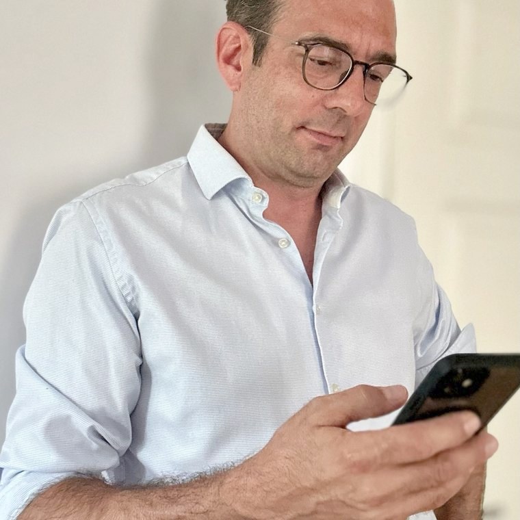 Thomas Kohns im hellblauen Hemd schaut auf sein Handy